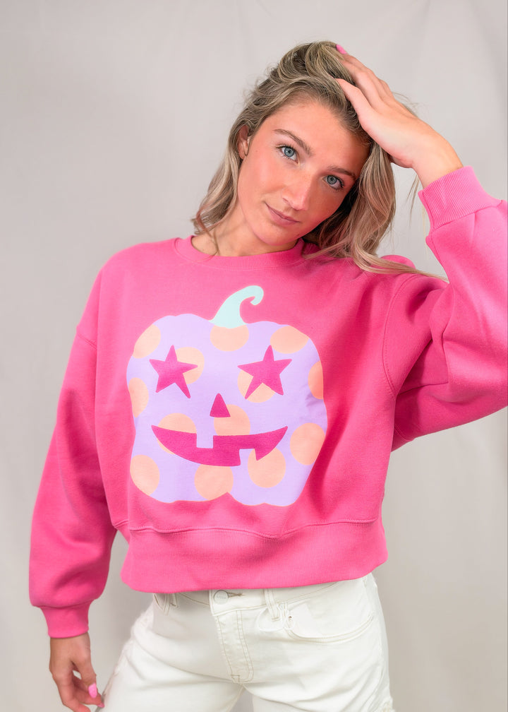 Woman wearing pink sweatshirt with purple polka dot pumpkin on front on plain background