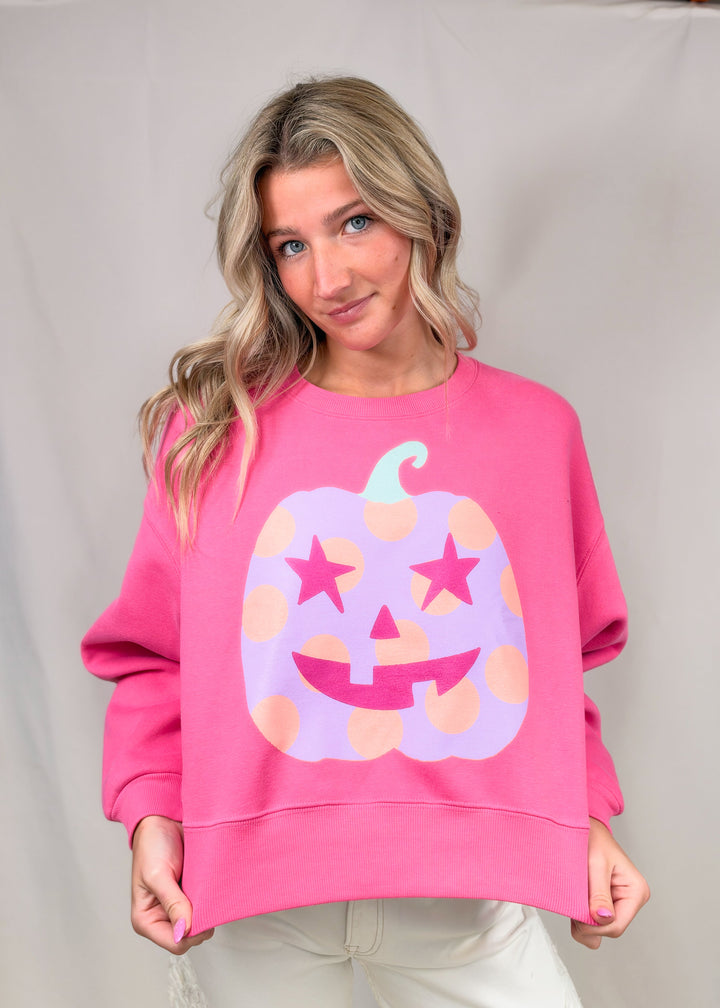 Woman wearing pink sweatshirt with purple polka dot pumpkin on plain background