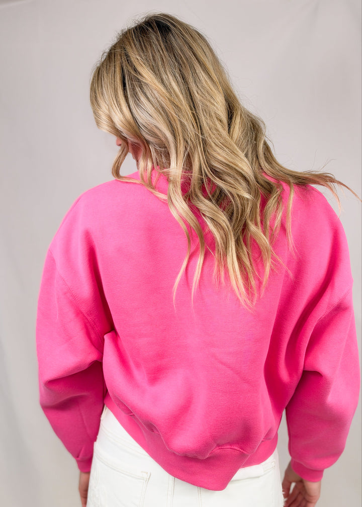 Woman shown from back wearing pink sweatshirt and white pants on plain background