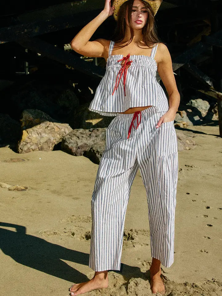 Woman in a striped outfit standing on a beach with rocks and sand in the background