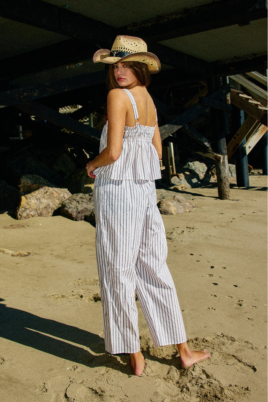 Person wearing a blue and white striped outfit with wide-leg pants on a beige background