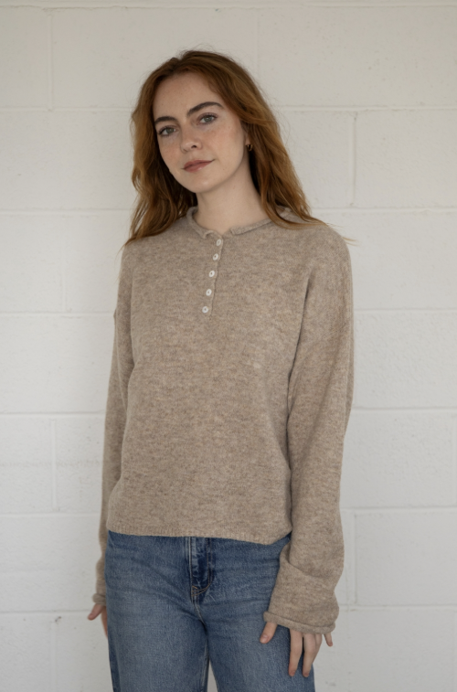 Woman wearing taupe sweater henley and jeans on plain background