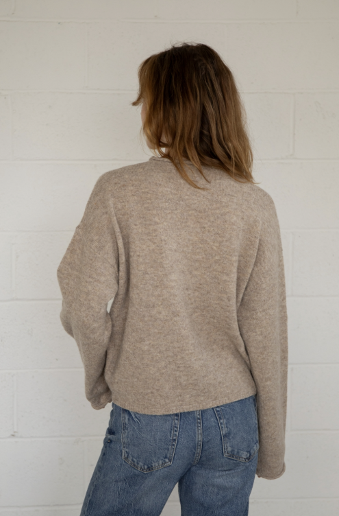 Woman shown from behind wearing taupe sweater and jeans on plain background