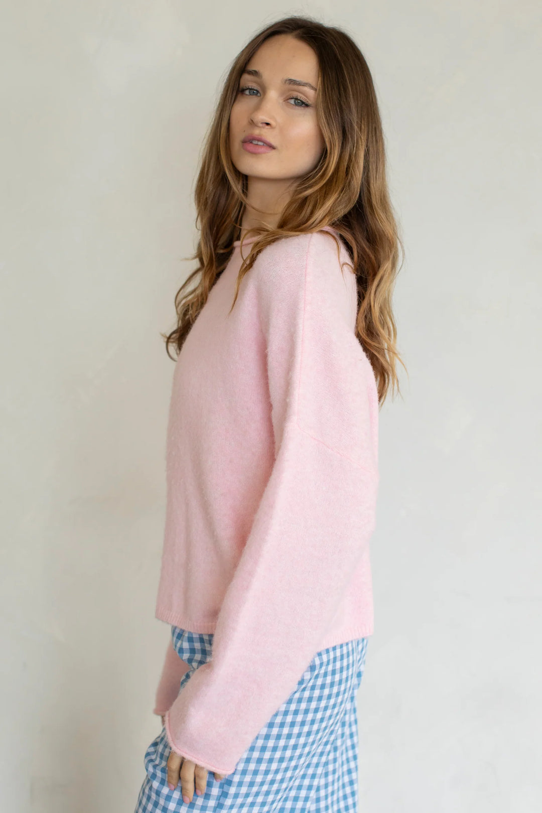 Woman wearing a pink sweater and blue checkered pants against a plain background