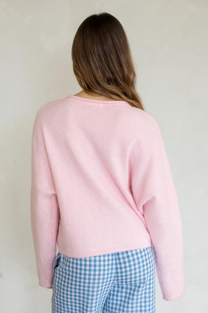 Person wearing a light pink sweater and blue checkered pants against a plain background