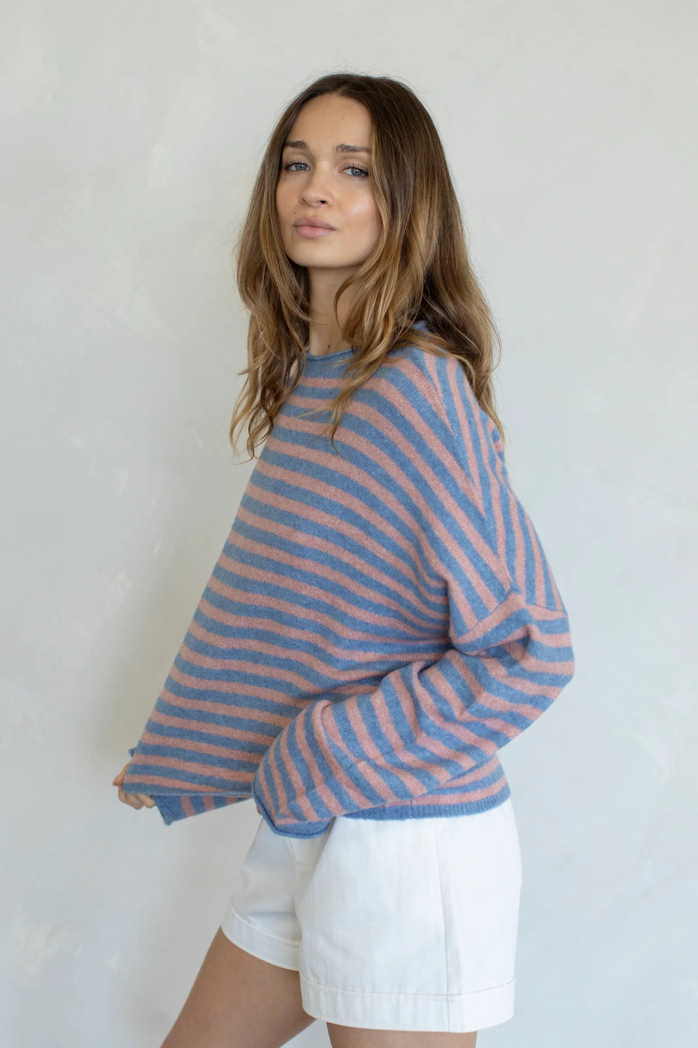 Woman wearing stripe sweater and white shorts on plain background