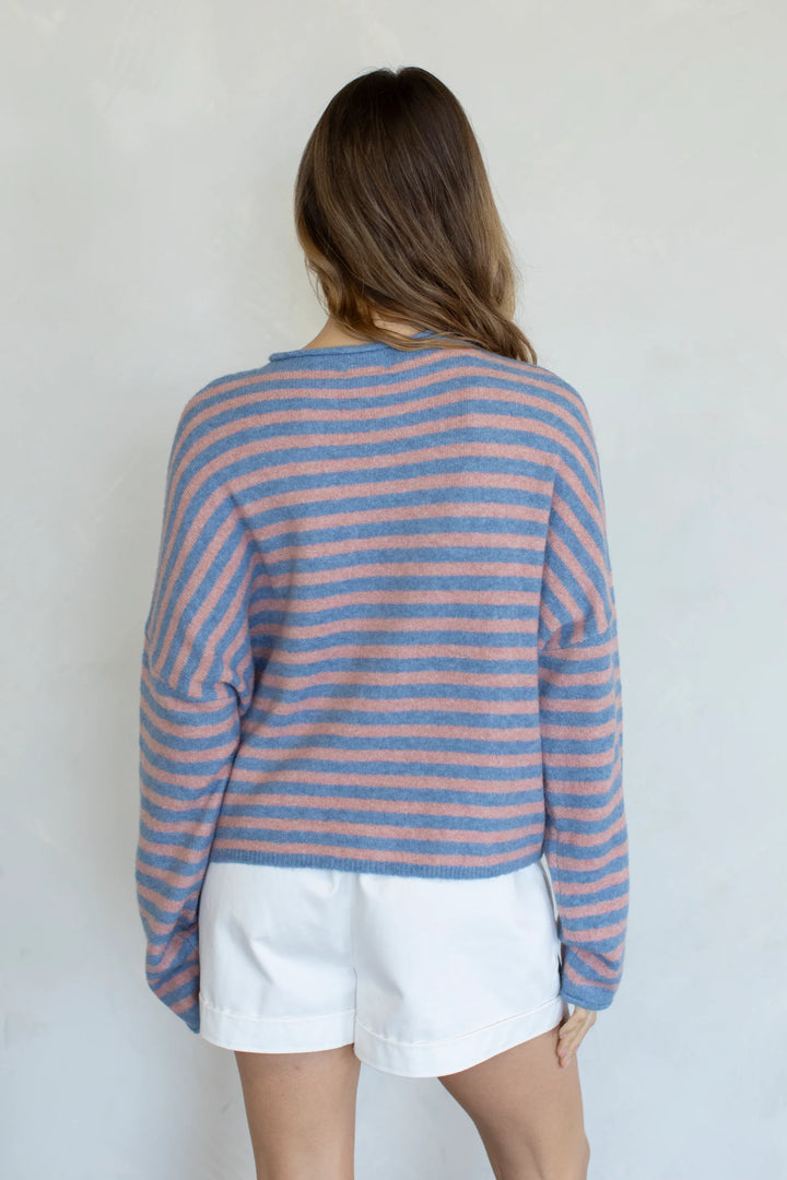 Back of woman wearing stripe sweater and white shorts on plain background
