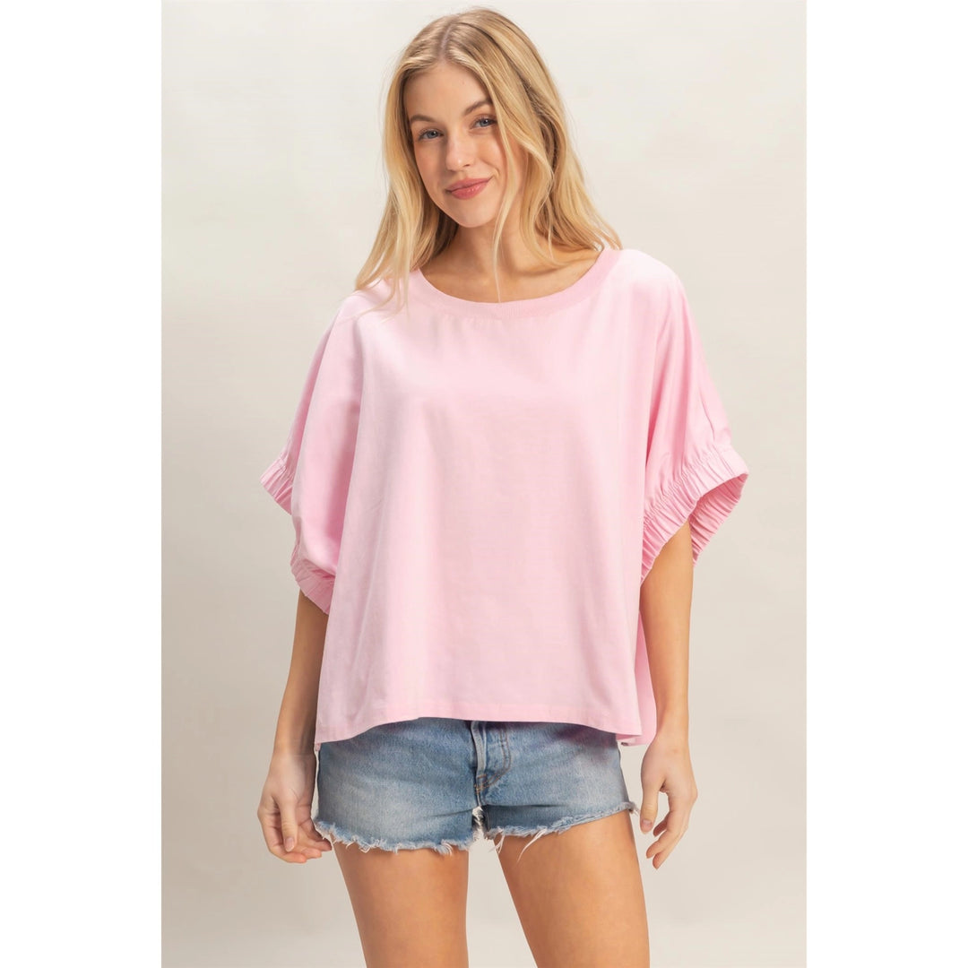 Woman wearing a pink oversized top and denim shorts on a plain background