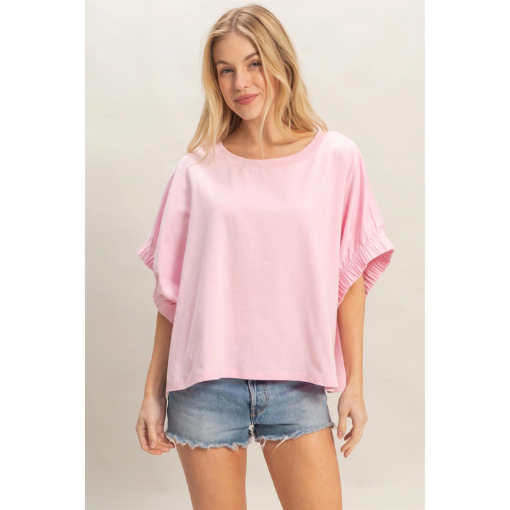 Woman wearing a pink oversized top and denim shorts on a plain background