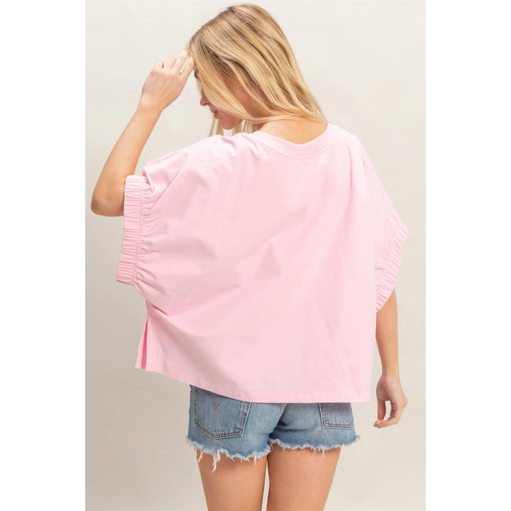 Woman wearing a pink oversized top and denim shorts on a plain background