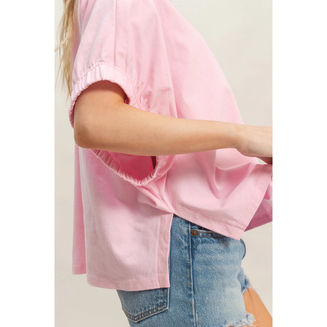 Person wearing a pink blouse and denim shorts on a plain background
