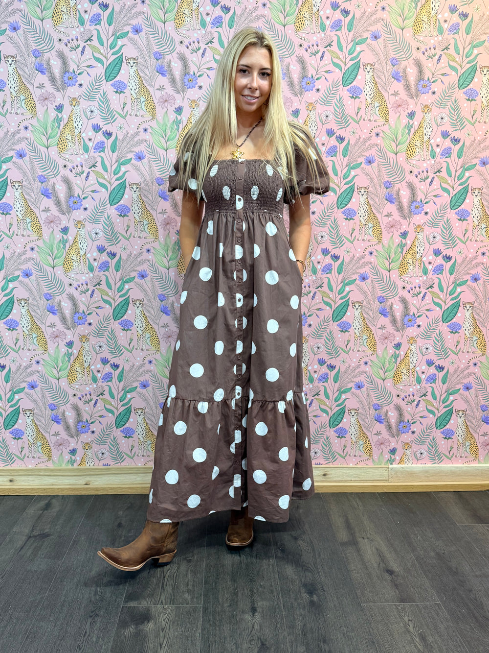 Woman wearing a brown polka dot dress standing in front of a patterned wall.