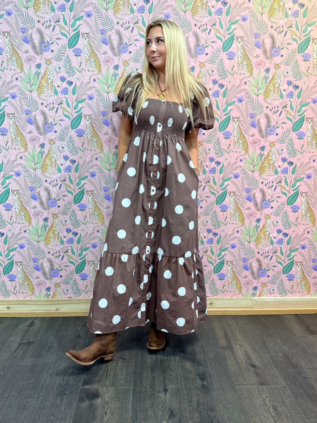 Woman wearing a brown dress with white polka dots against a patterned wall.
