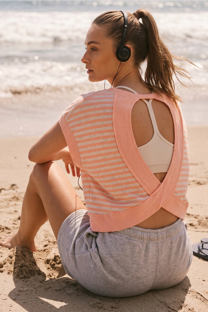 Woman sitting on the beach wearing a pink and white striped top, gray shorts, and headphones.