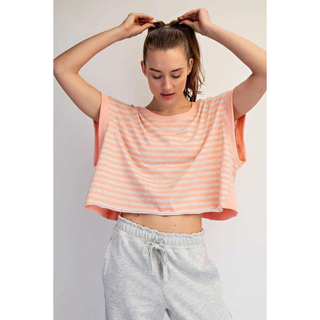 Woman wearing a peach and white striped top and gray sweatpants against a plain background