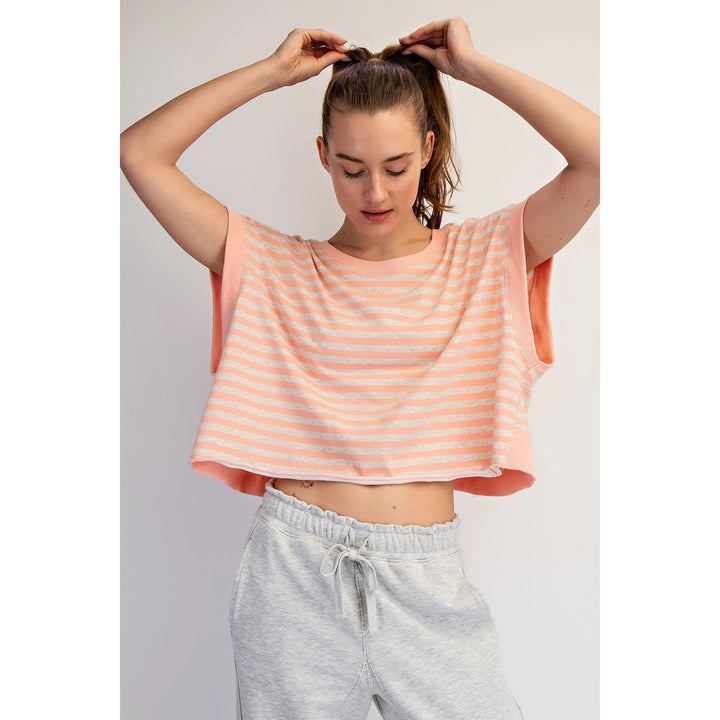 Woman wearing a peach and white striped top and gray sweatpants against a plain background