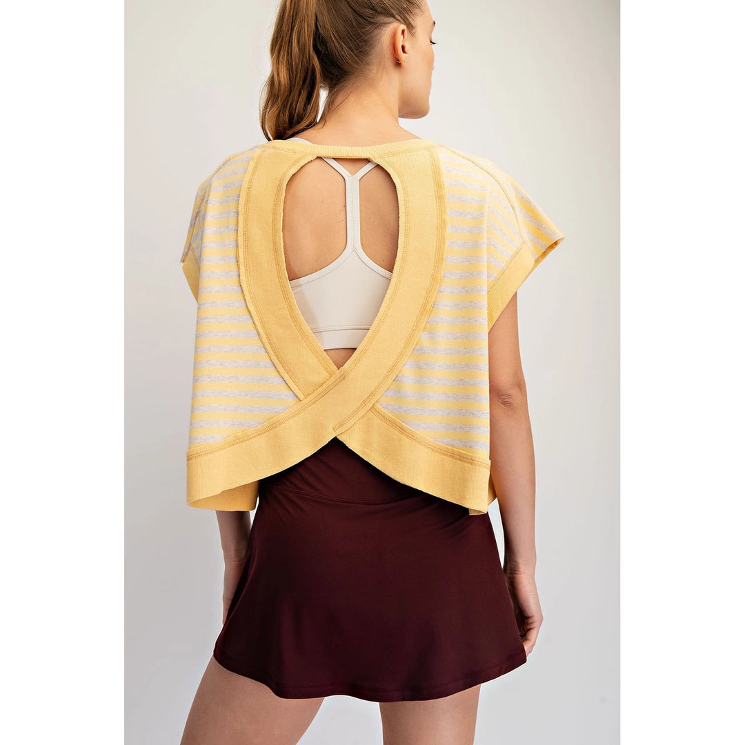 Woman wearing a yellow open-back top over a white tank top with a burgundy skirt on a light gray background