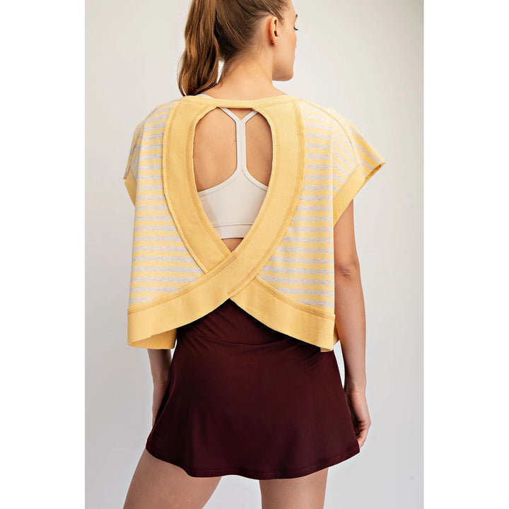 Woman wearing a yellow open-back top over a white tank top with a burgundy skirt on a light gray background