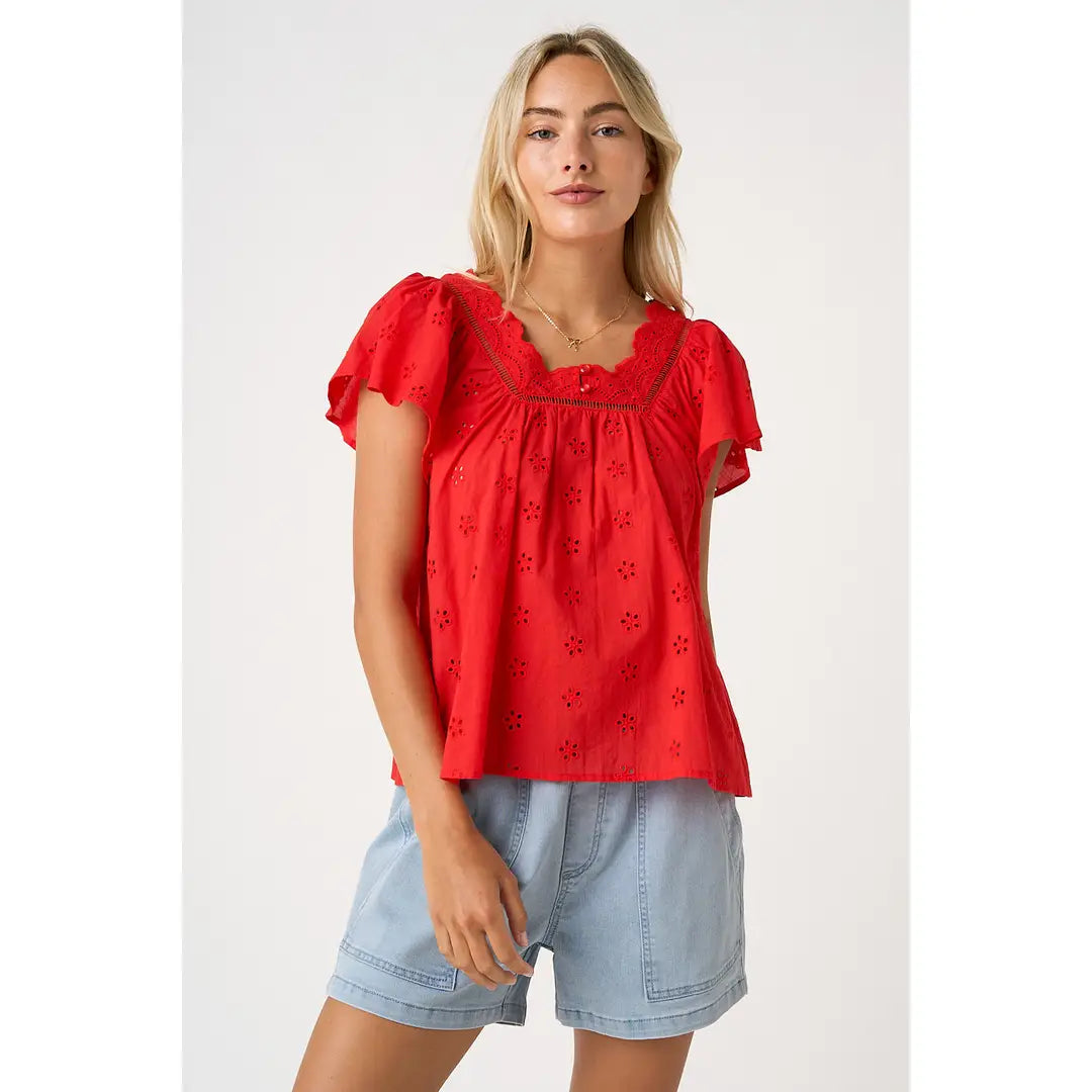 Woman wearing a red blouse with floral patterns and light blue shorts on a white background