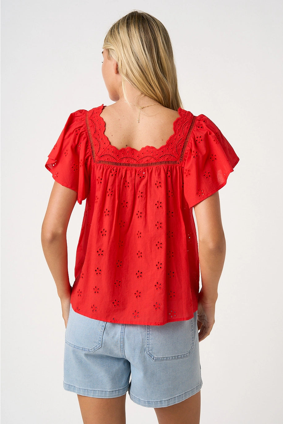 Woman wearing a red blouse with lace details and light blue shorts on a white background