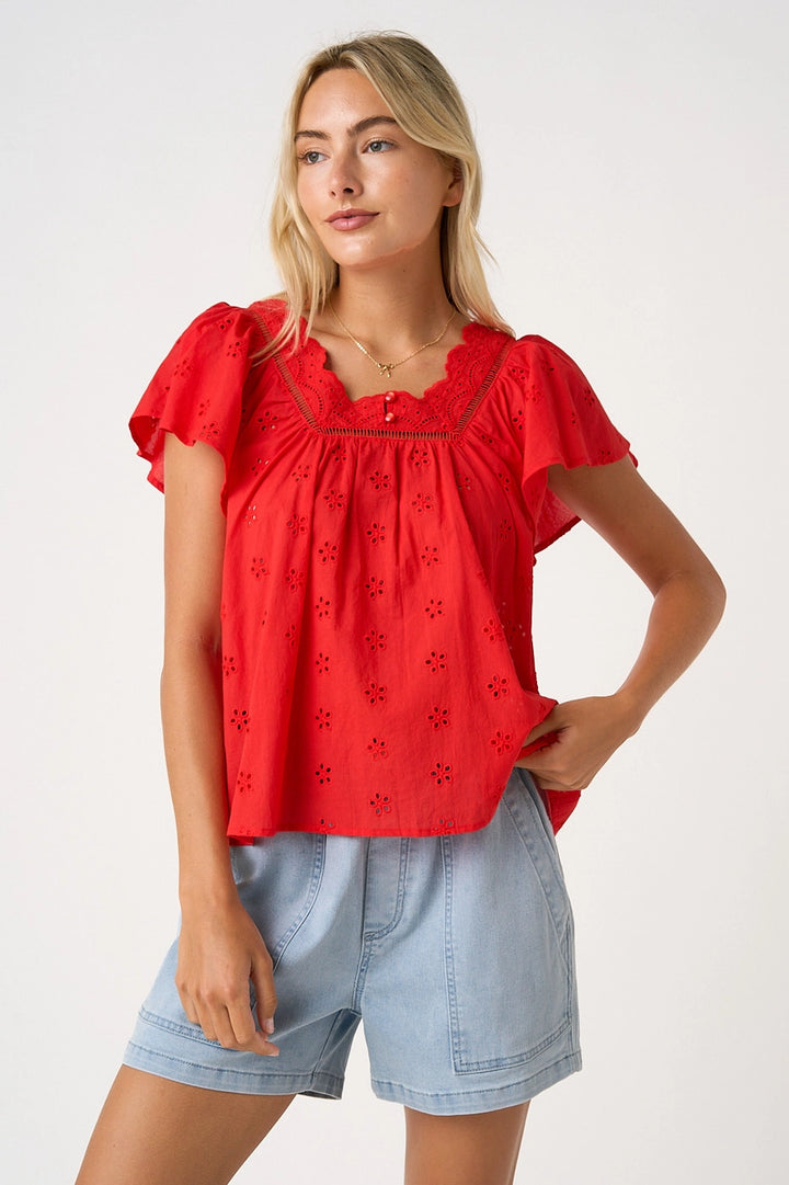 Woman wearing a red blouse with floral embroidery and light blue shorts on a white background