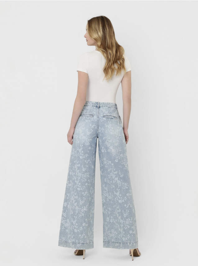 Woman wearing light blue floral pants and a white top on a plain background