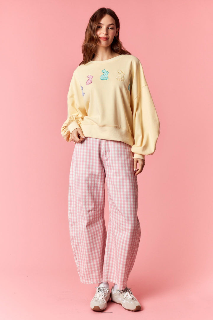 Woman wearing a yellow sweatshirt with colorful bear designs and pink checkered pants on a pink background