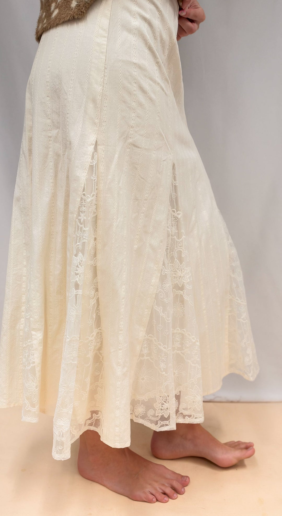 Woman shown from side view wearing lace detail maxi skirt on plain background