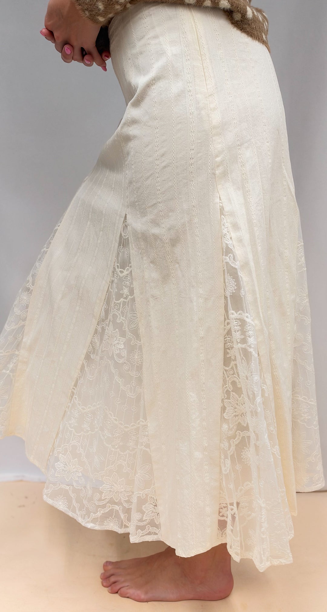 Woman shown from side view wearing lace detail maxi skirt on plain background