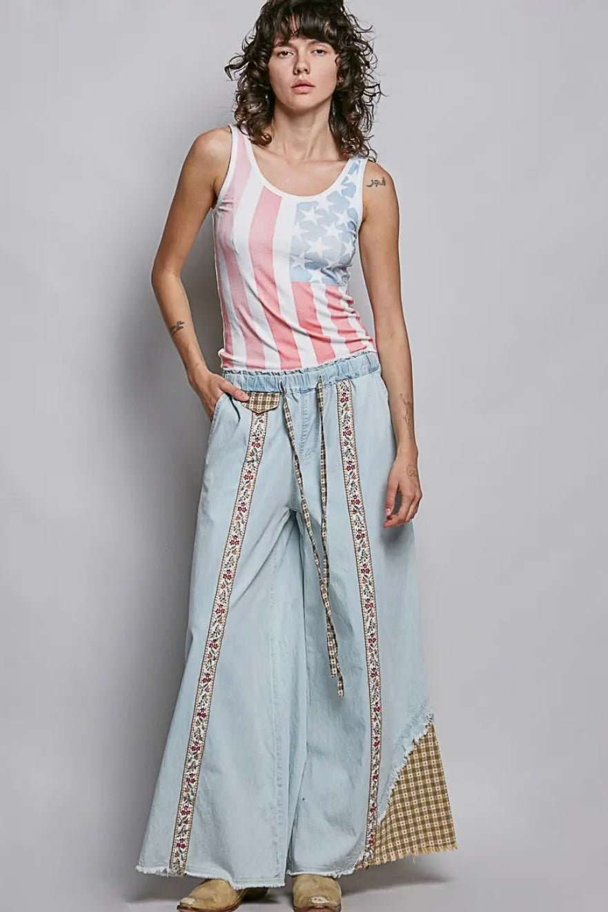 Woman wearing a sleeveless top with an American flag design and light blue pants with patterned trim.