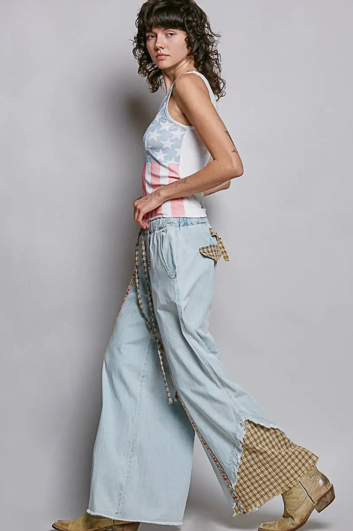 Woman wearing a sleeveless top and light blue jeans with a plaid pattern on a plain background