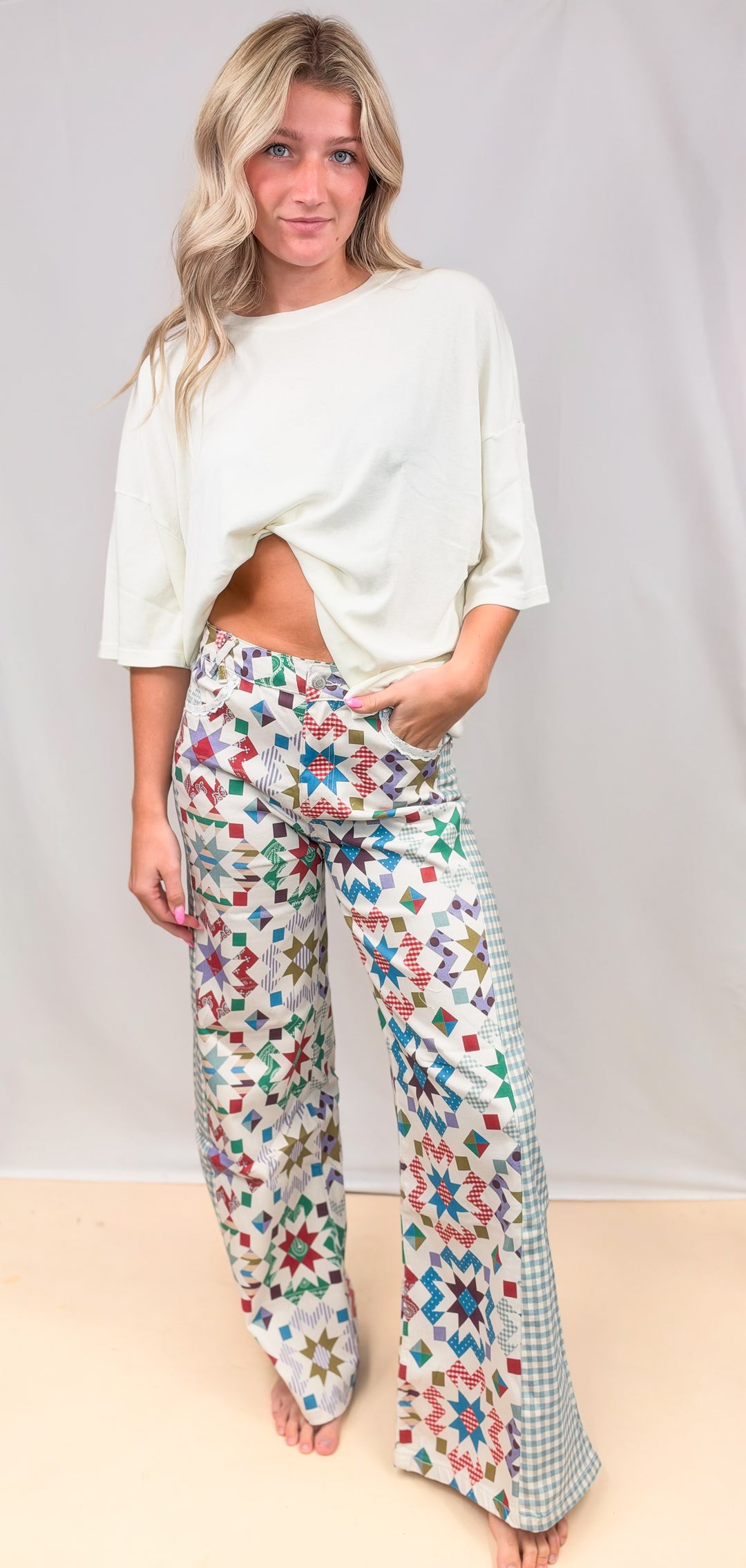Woman wearing quilted pattern pants with gingham details and cream top on plain background