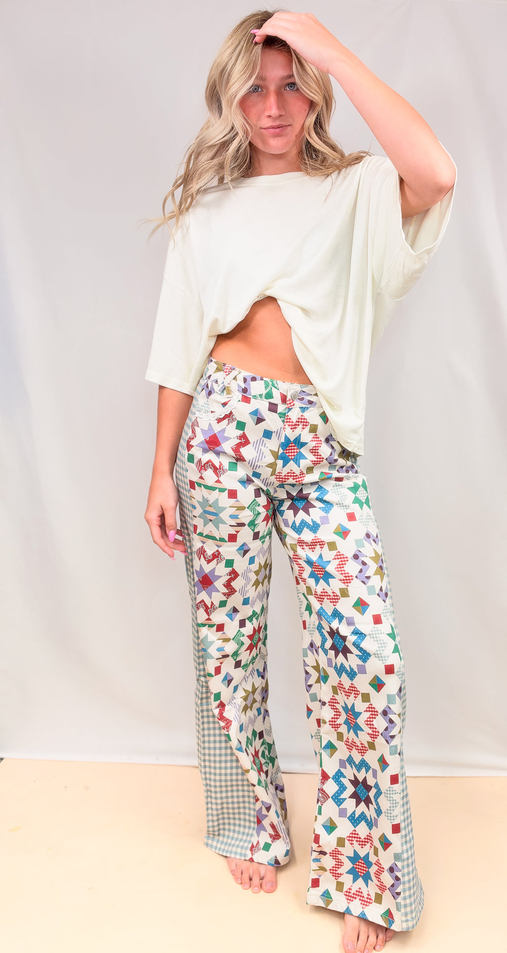 Woman wearing quilted pattern pants with gingham details and cream shirt on plain background