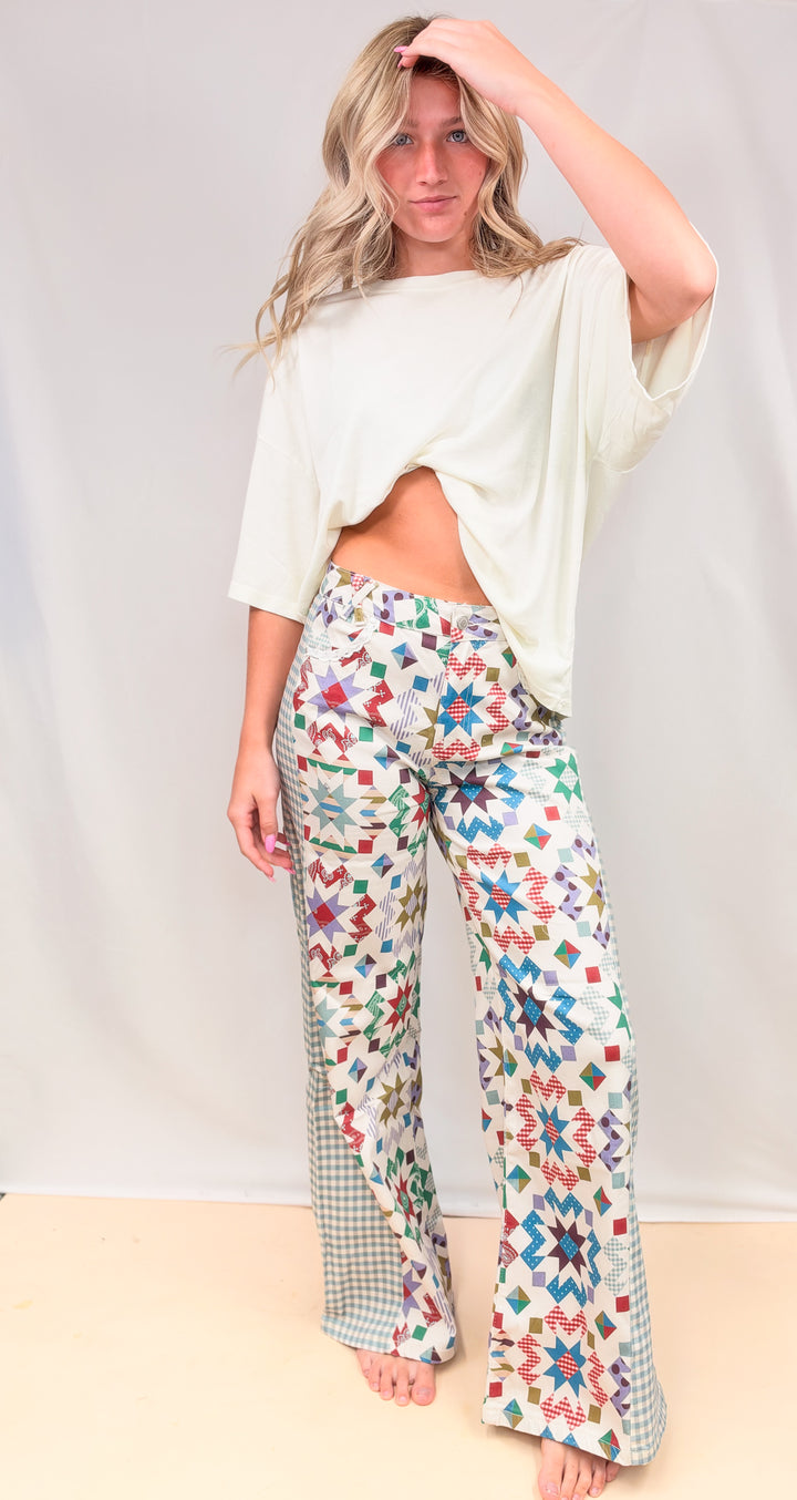 Woman wearing quilted pattern pants with gingham details and cream shirt on plain background