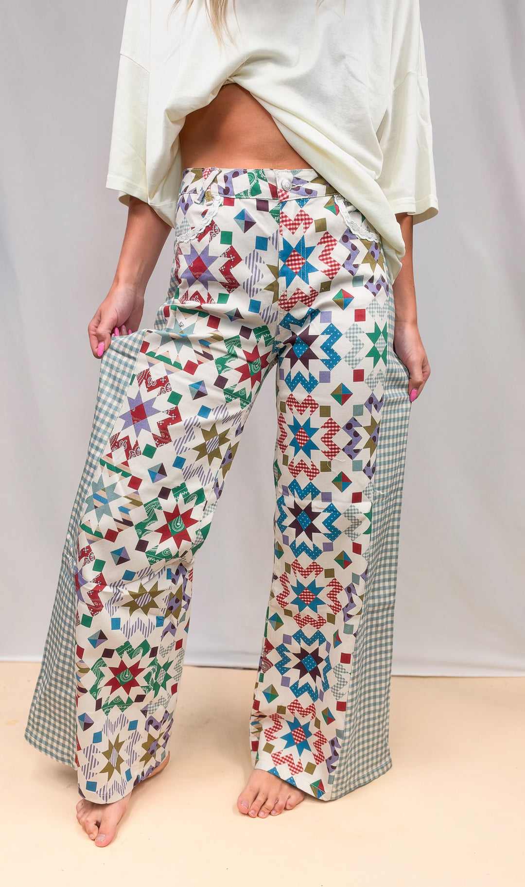 Woman wearing quilted pattern pants with gingham details and cream shirt on plain background