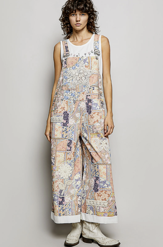 Woman wearing floral patchwork overalls with white tank on plain background