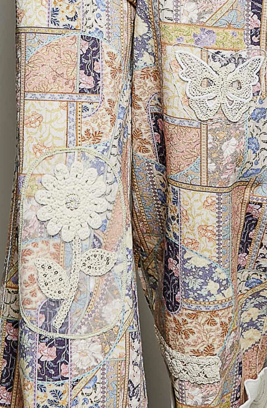Close-up of a patchwork-patterned garment featuring floral lace appliques, patchwork fabric panels, and embroidered details in soft pastel tones including beige, pink, blue, and cream.