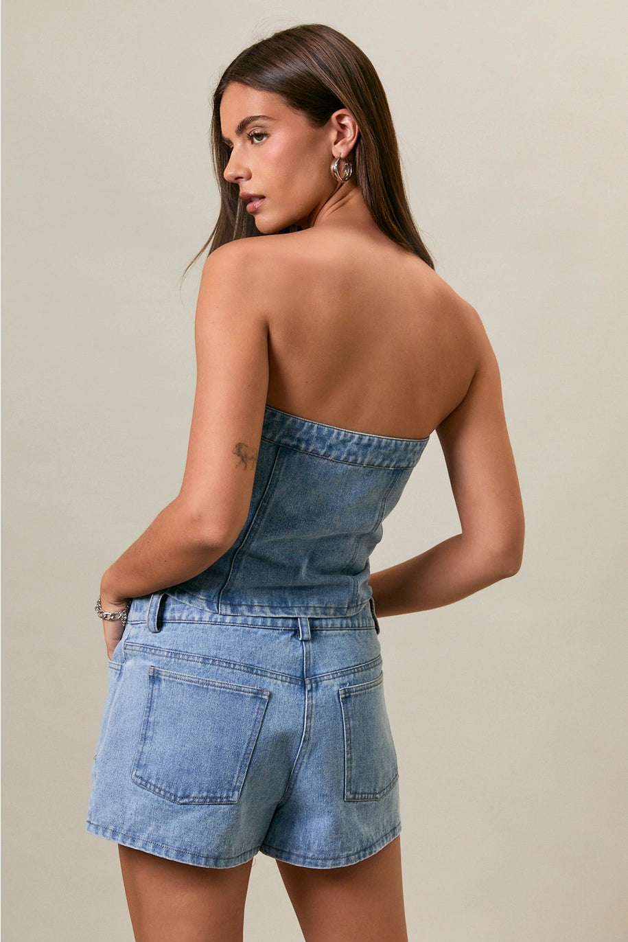 Woman wearing a denim strapless top and shorts on a beige background