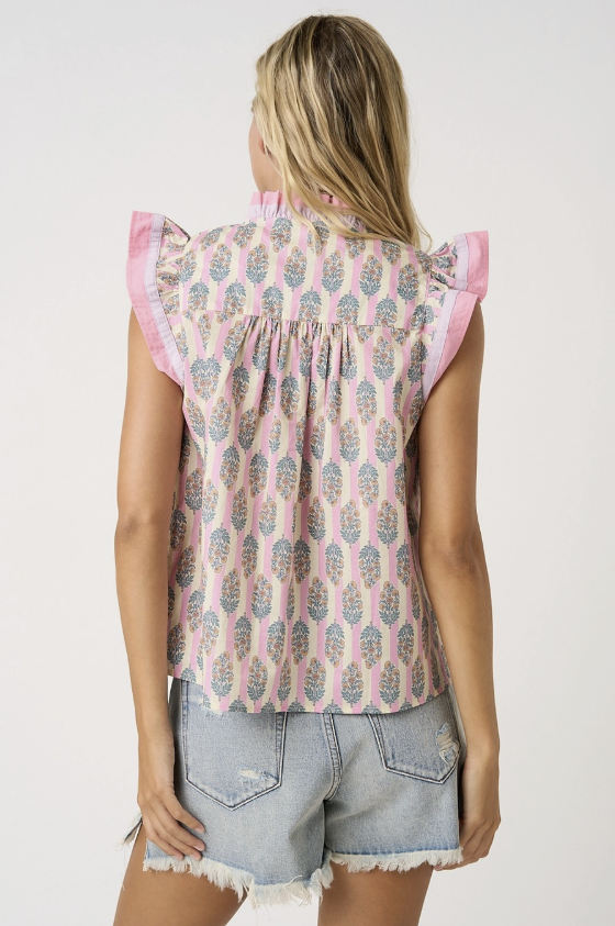 Woman wearing a sleeveless patterned top with ruffled sleeves on a plain background
