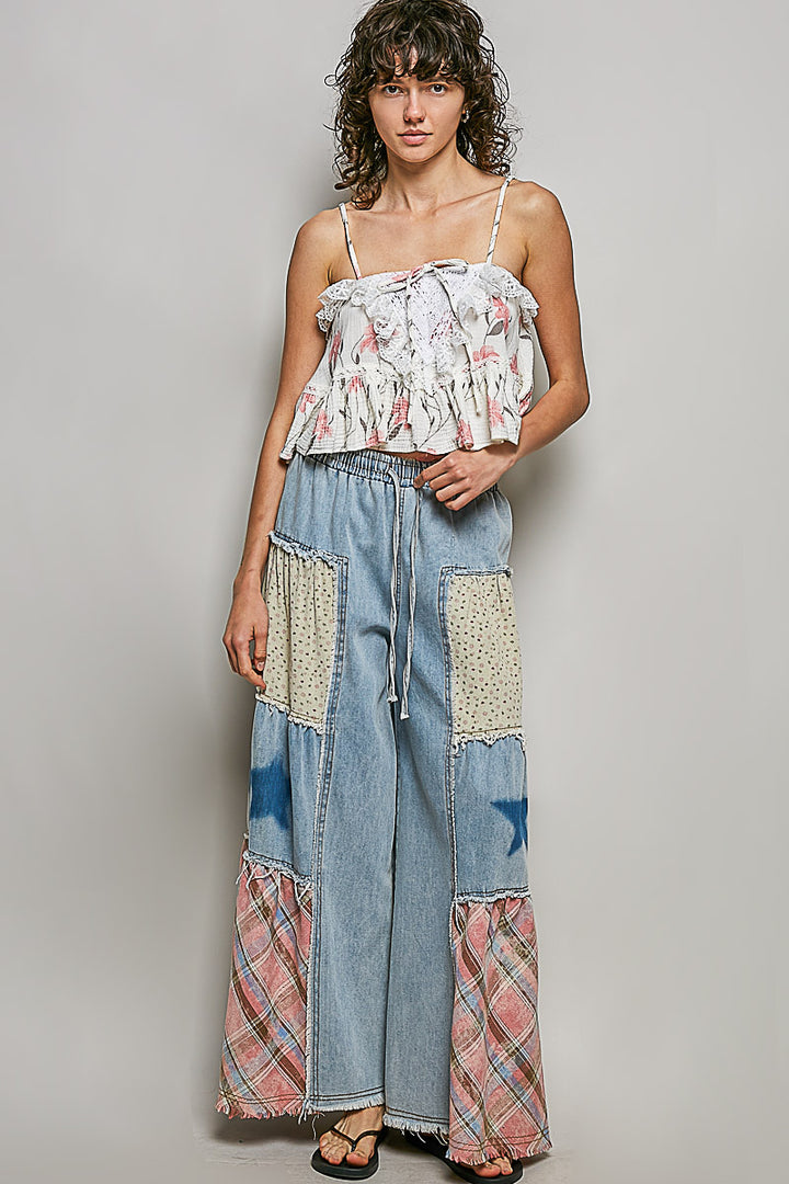 Woman wearing a floral top and patchwork jeans against a plain background
