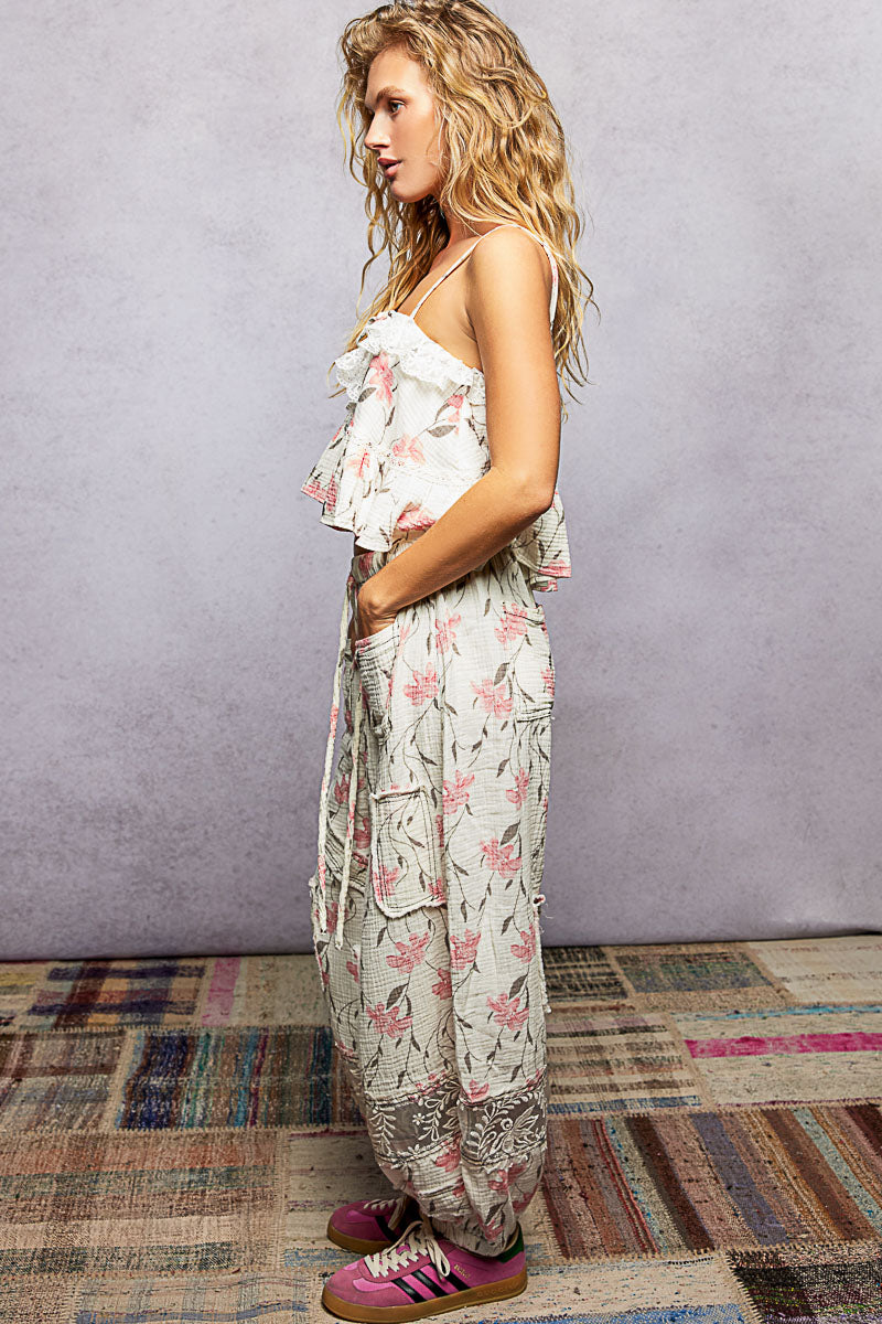 Woman wearing a floral cami and pants and sneakers on a textured floor with a gray wall background