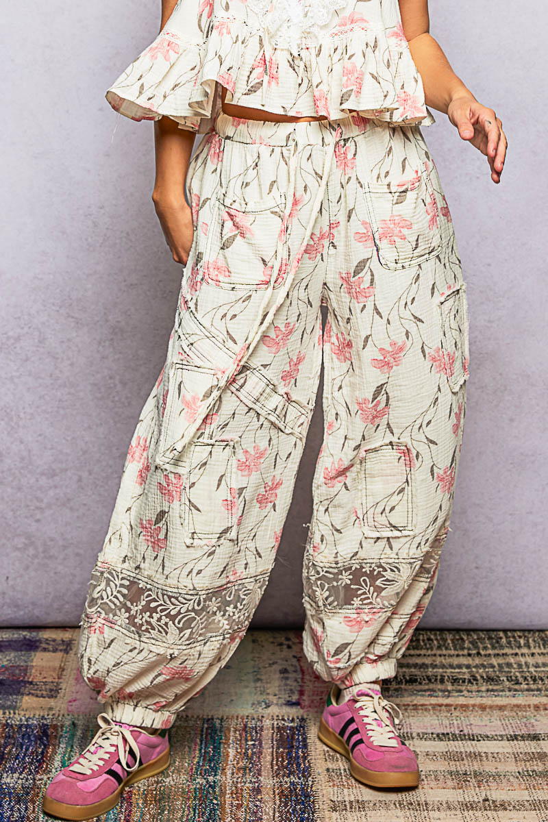 Person wearing floral pants and pink sneakers on a plain background