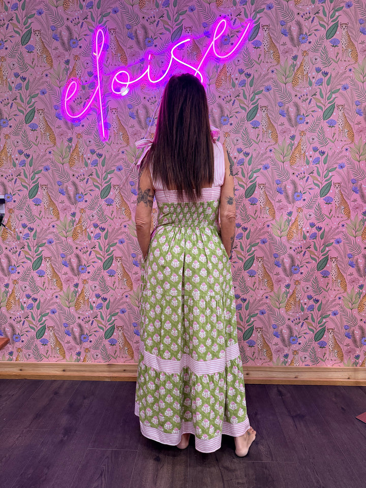 Back of woman wearing green and pink floral dress on pink floral background