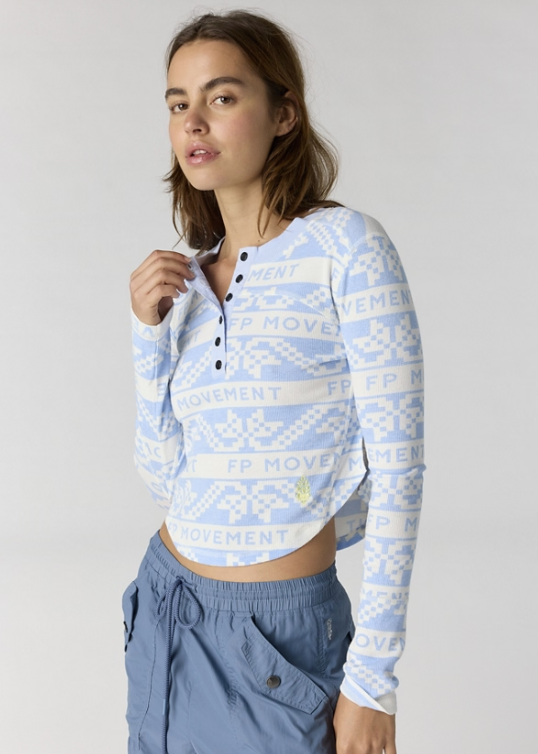Woman wearing blue and white printed henley top with blue pants on plain background