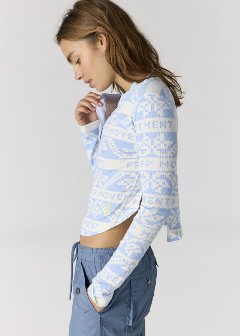 Woman wearing blue and white printed henley top with blue pants on plain background