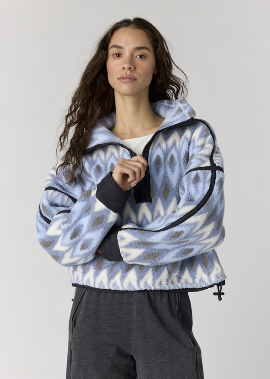 Woman modeling printed fleece in blues with gray pants on plain background