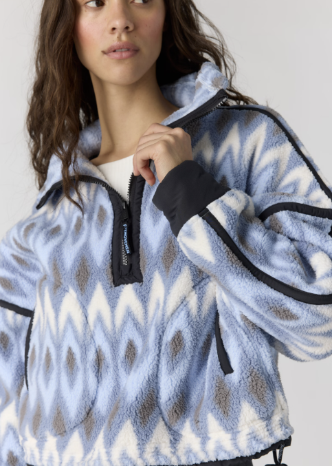 A woman wearing a light blue and white patterned fleece quarter-zip pullover with black trim, shown in a close-up studio shot.