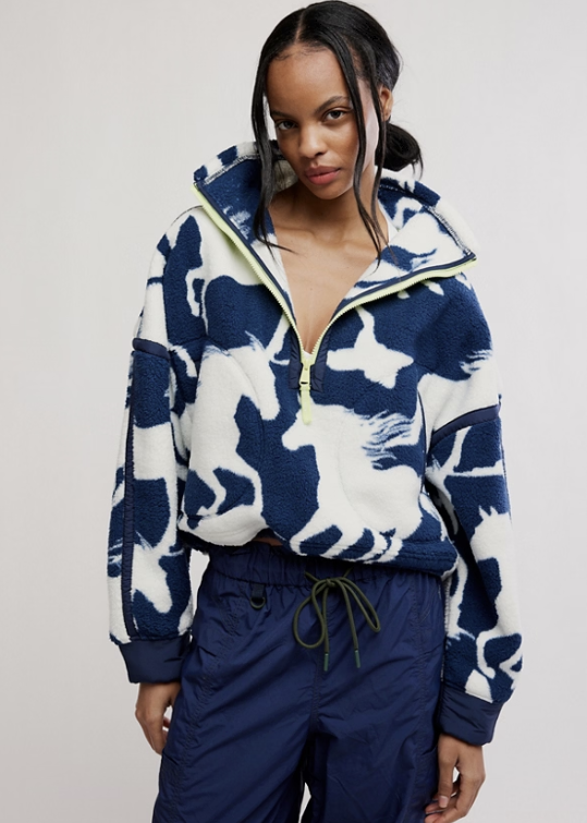 Woman wearing navy blue with white horses detail fleece jacket with blue pants on plain background