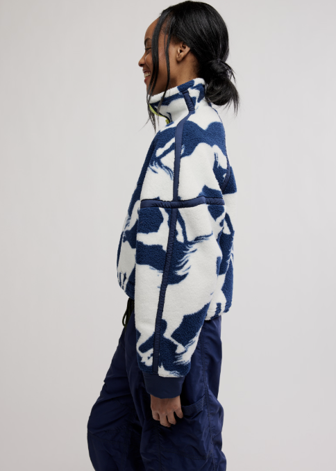 Woman wearing navy and white horse detail jacket with blue pants on plain background