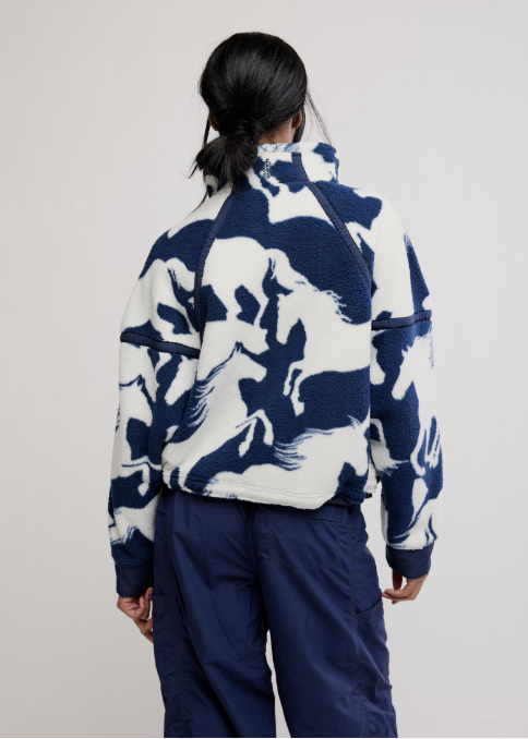 Woman shown from back wearing navy fleece jacket with white horse detail and blue pants on plain background